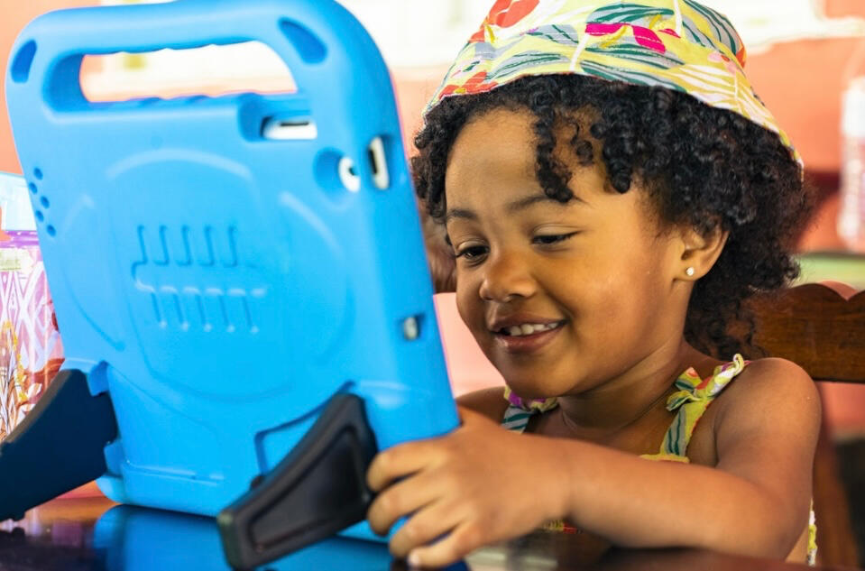 alt= Smiling young dark skinned girl with curls playing with an ACC device
