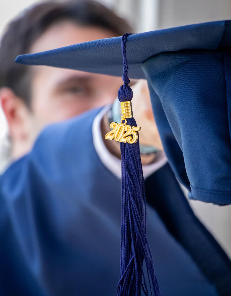 Male senior with black hair in navy blue cap and gown. From the tassel hangs a gold 25.