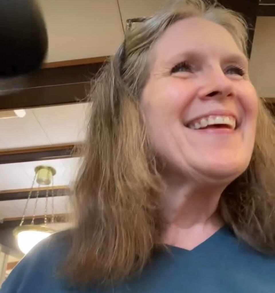A headshot of Donna Earnest smiling in a teal tee shirt working out in the gym.
