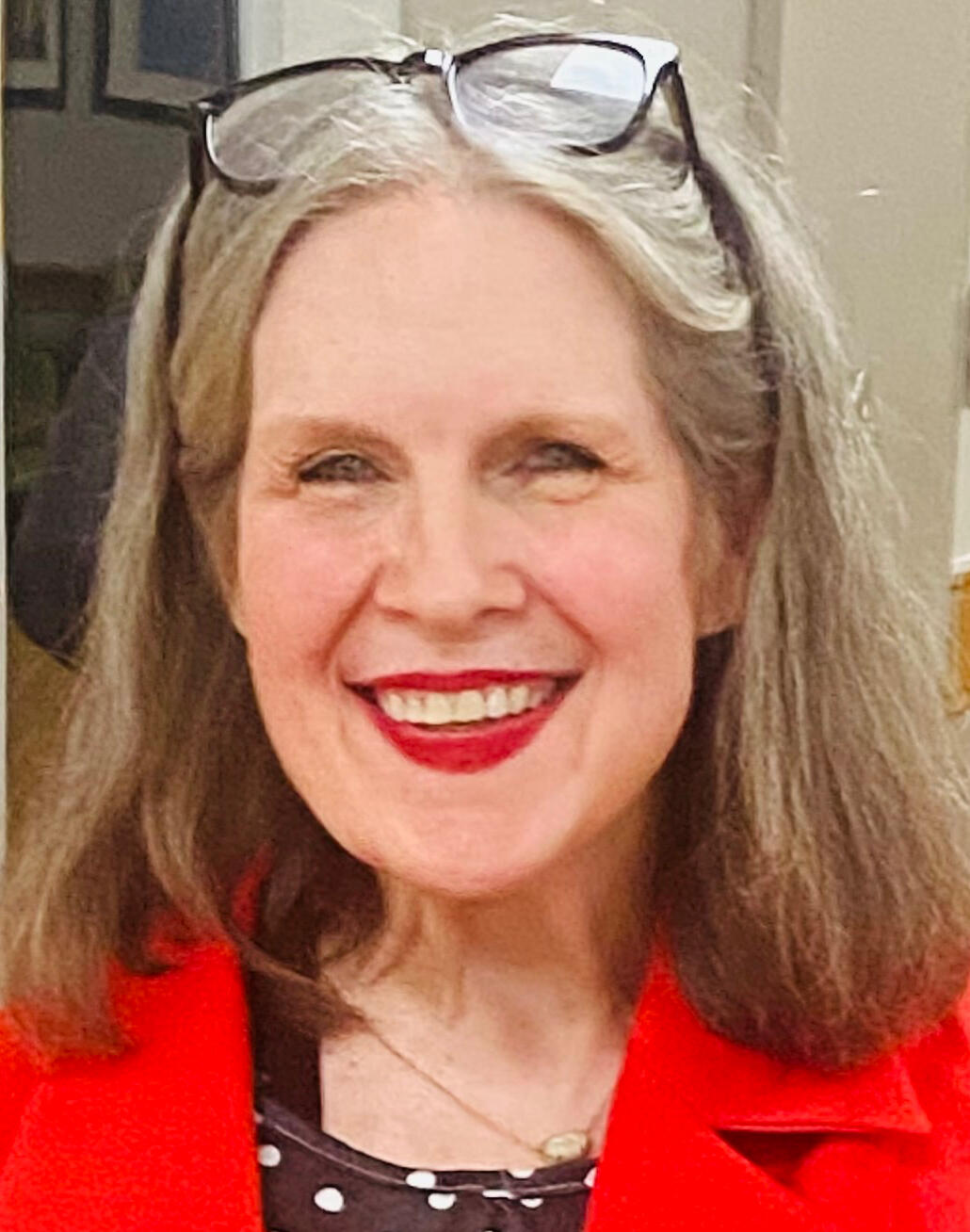 Casual photo of Refine Disabilities founder Donna Earnest. She is a white woman in her late 60’s, with shoulder length brown mixed with gray hair, wearing light makeup. She is smiling with joy at something off camera. She is indoors, wearing a dark teal te